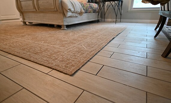 Closeup of click tile that looks like wood flooring, tan floor rug, sleigh bed and nightstand in the background.