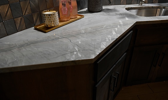 Closeup of basement kitchenette countertop of gray quartzite and backsplash of silver textured geometric wall tile that looks like metal tile.