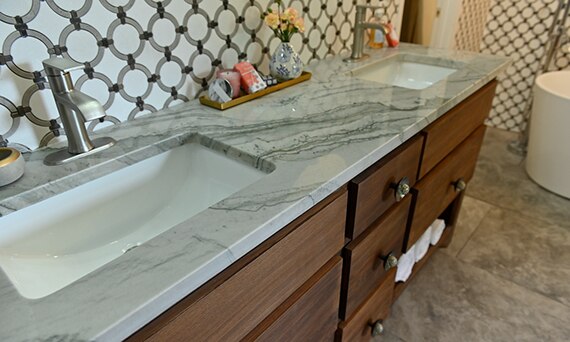 Bathroom with wood vanity with quartzite countertop, backsplash of white marble tile with gray rings, and gray marble look floor tile.