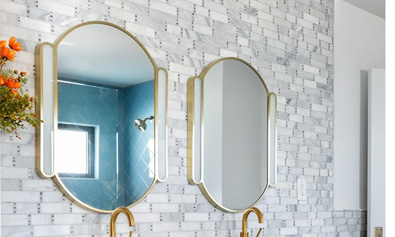 Closeup of bathroom backsplash with marble mosaic tile and dual lighted vanity mirrors.