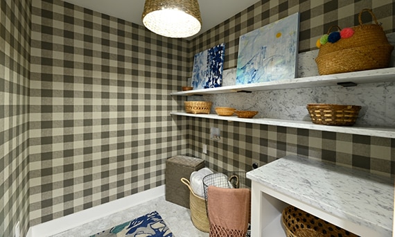 Laundry room with gray and white marble countertop and floating shelves, marble hexagon floor tile, and cream & gray plaid wallpaper.