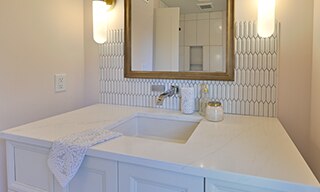 Bathroom vanity with peach walls, white picket tile backsplash, white quartz counter with undermount sink, wood frame mirror and dual wall sconces.