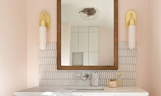 Bathroom vanity with peach walls, white picket tile backsplash, white quartz counter with undermount sink, wood frame mirror and dual wall sconces.