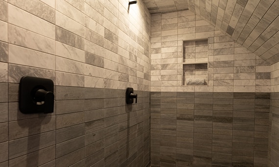 Large walk-in shower with white & gray marble subway tile on the top half of the walls, light & dark gray marble tile on the bottom half of the walls, and black fixtures.