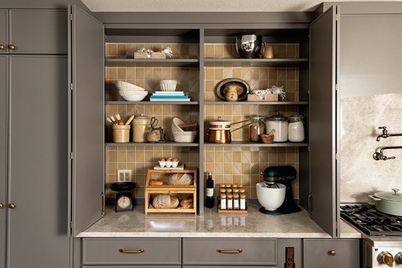 Kitchen cabinet with yellow mosaic walls and gray shelves adorned with various kitchen supplies.