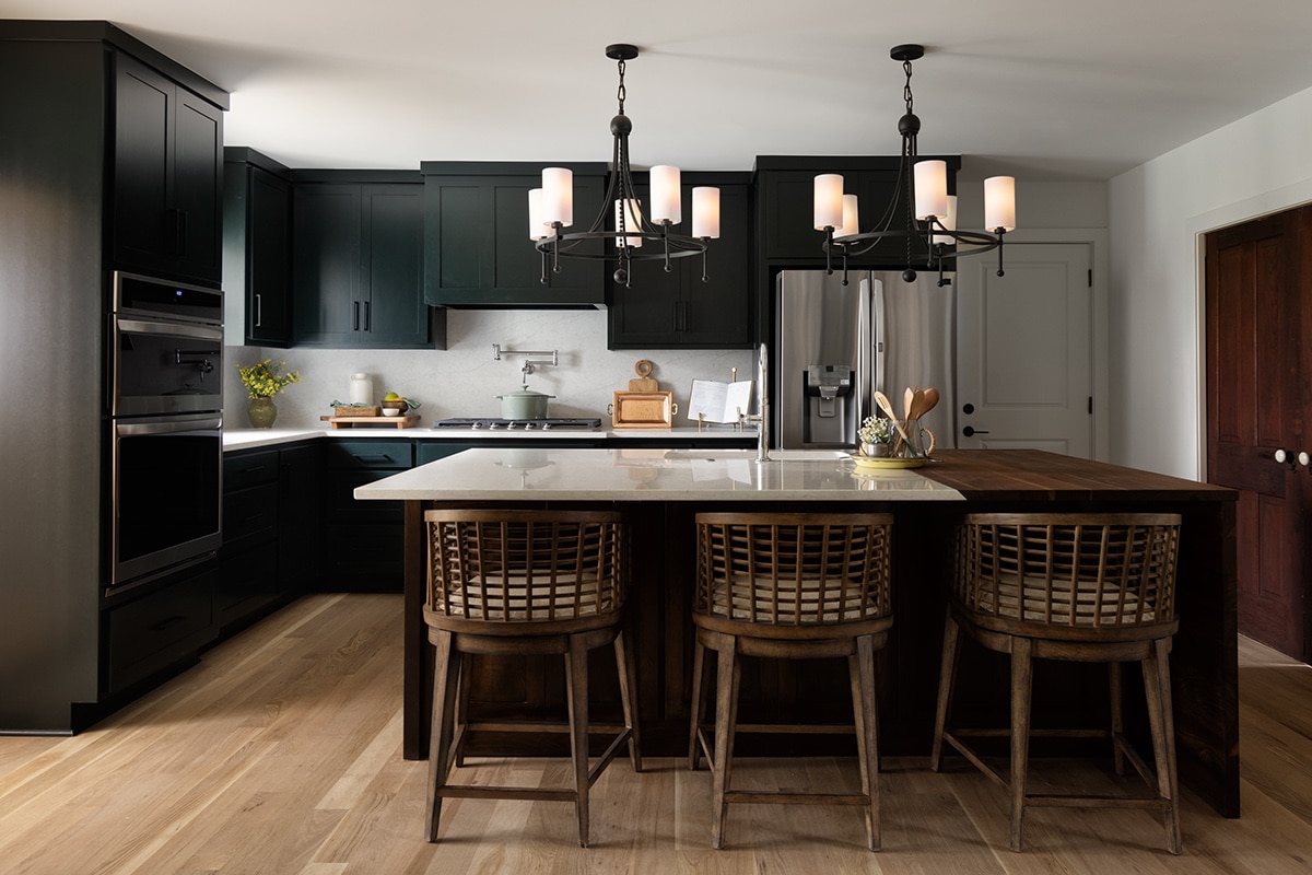 Kitchen with island in center, dark green cabinets, silver fridge, and a white quartz countertop and backsplash.