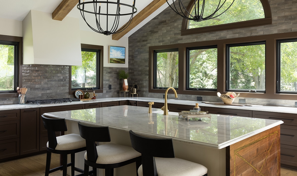 Kitchen with brown cabinets, light wood floors, white quartzite slab countertop, and gray undulated subway tiles on the walls.