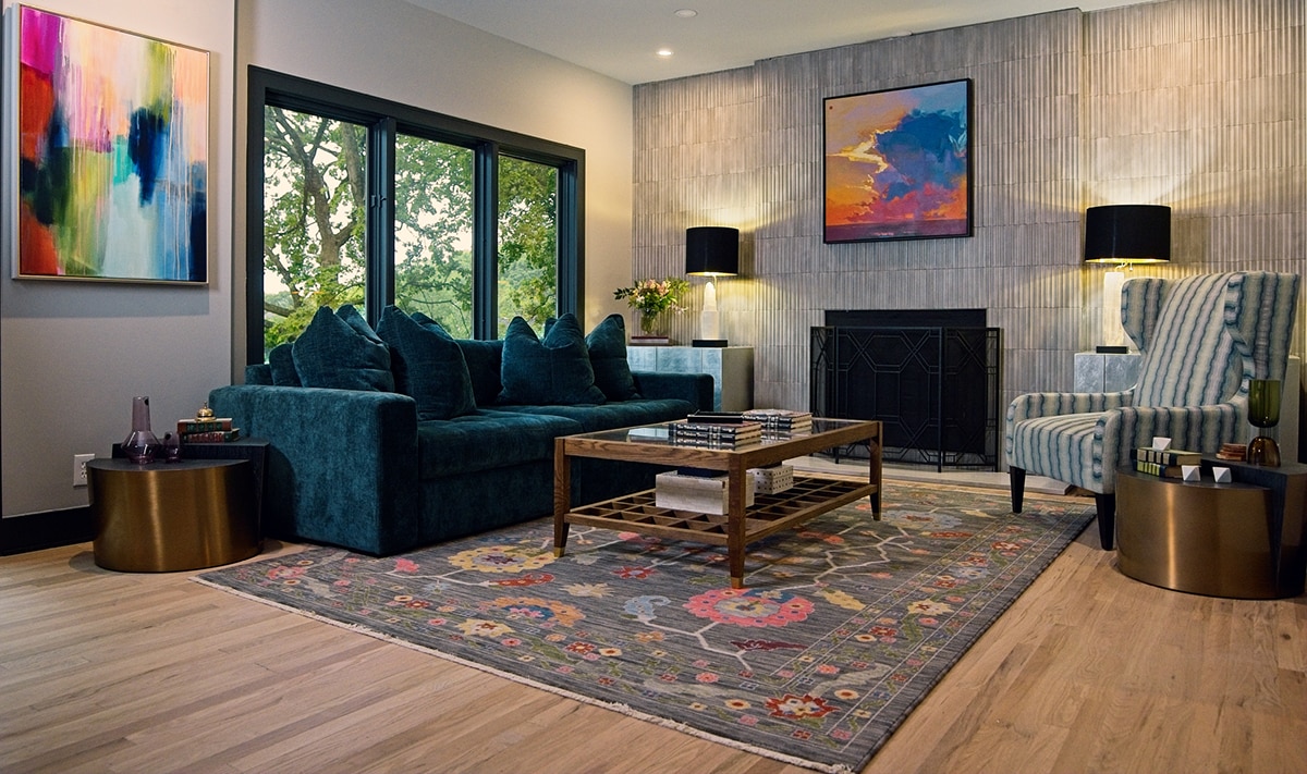 Living room with green couch, light wood floors and a gray fluted tile on the back wall and surrounding the fireplace.