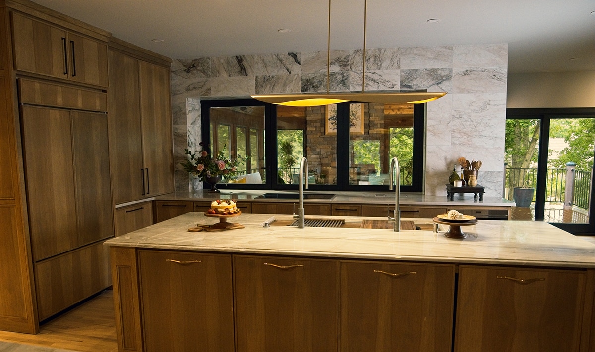 Kitchen with wood cabinets, a center island with a beige quartzite countertop, and a white marble look tile on the back wall.