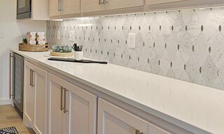 Butler’s pantry with white quartz countertop, white & gray marble mosaic backsplash with antique mirror accents, and white wash wood cabinets.