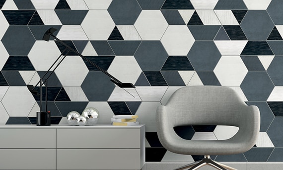 Eye-catching feature wall with white, gray and black hexagon tile, gray chair, gray credenza holding desk lamp and books, and gray floor tile.
