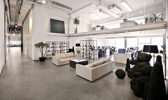 Office space with glass walls and lobby area with cream couches. Concrete-look twenty-four by twenty-four inch porcelain tiles on the floor.