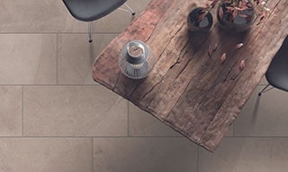 Bird’s eye view of rough wood table, chair, vase holding dried branches, tan floor tile that looks like stone.