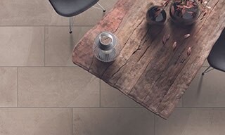 Bird’s eye view of rough wood table, chair, vase holding dried branches, tan floor tile that looks like stone.