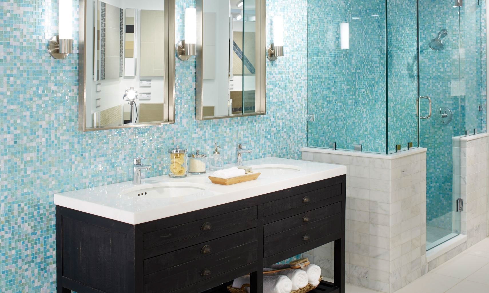 Bathroom with vanity wall and shower walls covered with blue, green, and white iridescent mosaic tile, dark wood vanity with dual sinks and mirrors.