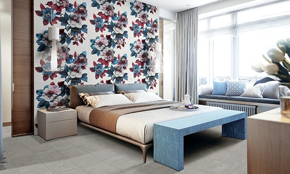 Bedroom with white slab wall tile with large white, blue, and cranberry red flowers, platform king size bed with beige & blue bedding, and blue footboard.