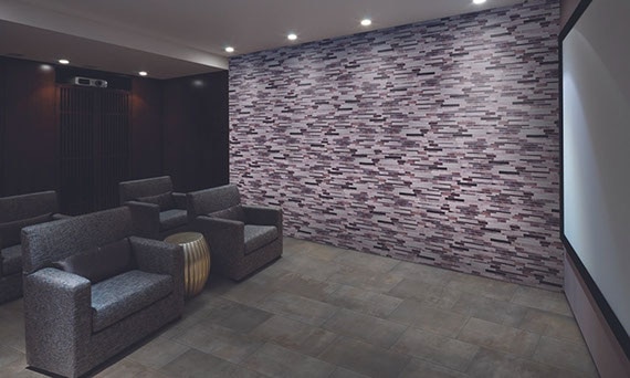 Media room with purple & lilac glass mosaic feature wall, mounted projector, projector screen, gray stone look floor tile, and 4 gray recliners.