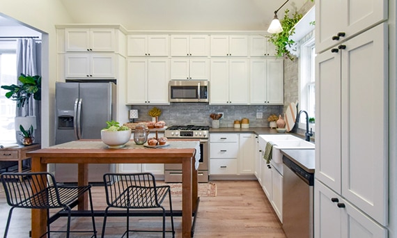 Kitchen with brown quartz countertops, cream cabinets, gray subway tile backsplash, butcherblock island, and stainless steel kitchen appliances.