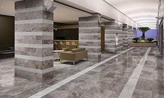 Hotel corridor with silver gray limestone on the floors, gray limestone columns with white limestone stripes, hotel bar with tan sofa & bar stools.