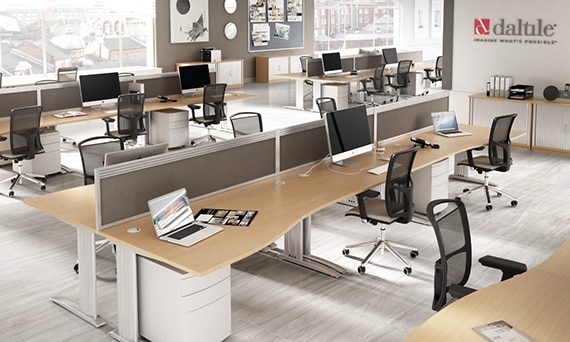 Open concept office with gray stone look floor tile, black rolling chairs, wood top desks holding laptops and monitors with keyboards.