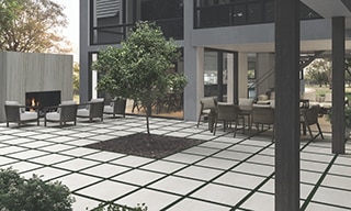 Courtyard of two-story house with dining table & chairs, outdoor fireplace & seating area, and tree in the middle of white 2CM pavers.