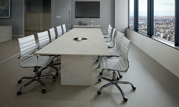 Conference room with gray fabric look floor tile, long cream quartz table with gray veining, cream leather chairs, windows with a city view.