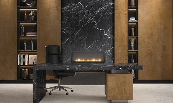 Home office with bookshelves of metallic looking porcelain slab and fireplace surround of black marble look porcelain slab, and desk made of porcelain slab that looks like black marble.