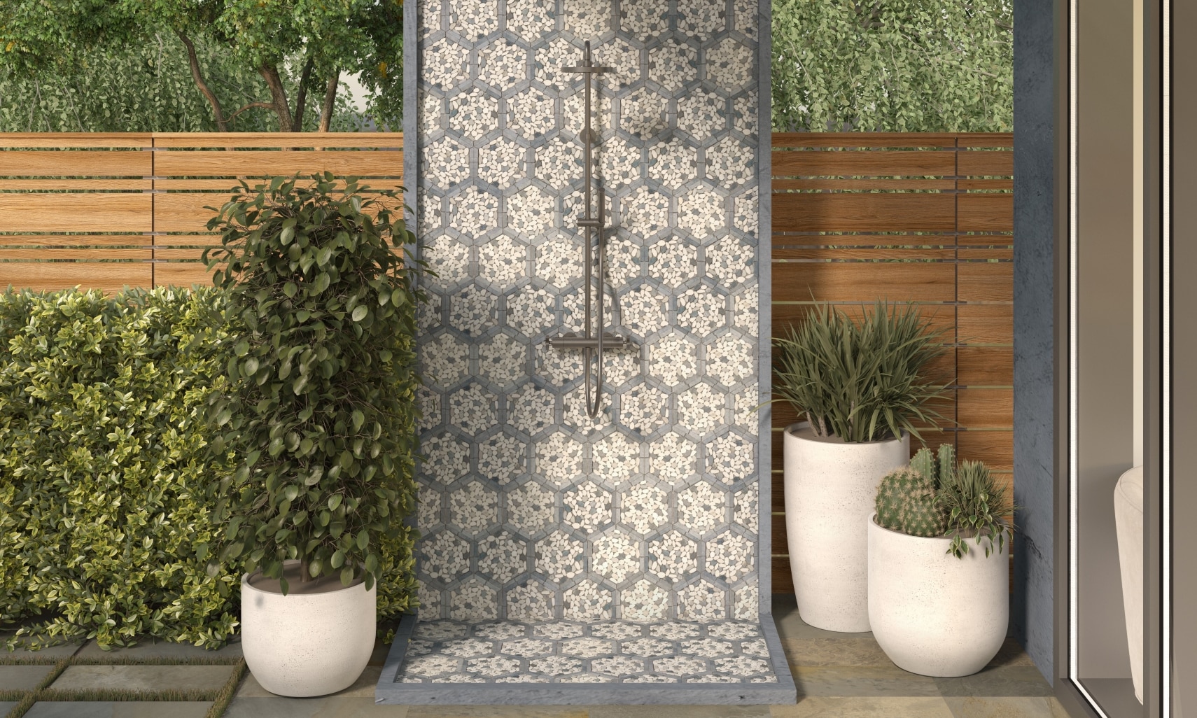 Outdoor shower wall and floor with white & beige pebble mosaic tile with gray hexagon frame, surrounded by shrubbery and potted plants.