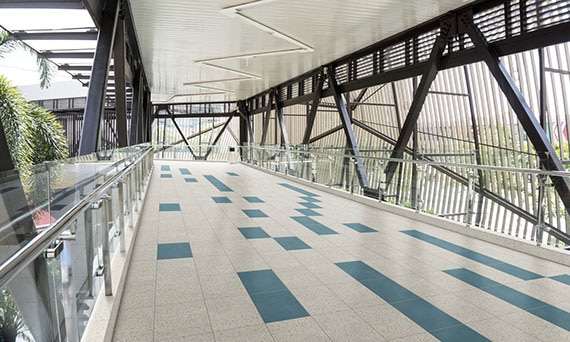 Interior of skywalk with gray and blue concrete look floor tile, glass & metal railing, black metal rafters and beams.
