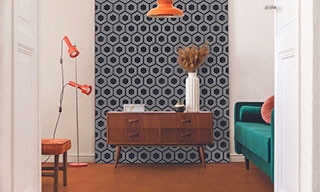 Eclectic style room with retro wood side table in front of black & white hexagon wall tile, orange concrete look tile floor, and green velvet loveseat with coral throw pillow.