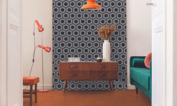 Eclectic style room with retro wood side table in front of black & white hexagon wall tile, orange concrete look tile floor, and green velvet loveseat with coral throw pillow.