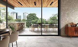 Restaurant indoor and outdoor dining room with gray stone-look floor tile, herringbone wall tile, natural quartzite waterfall island, and view of city skyline.