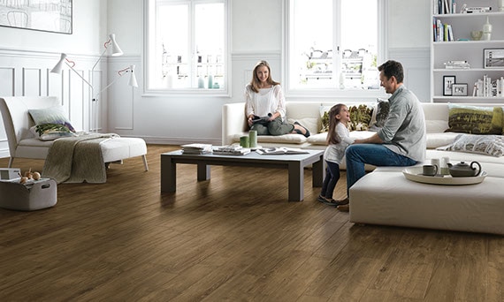 Living room with wood-look porcelain tile floors, clean-lined cream furniture, and man, woman, and child playing together.