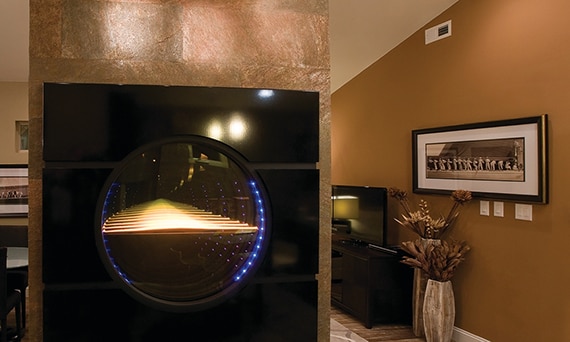 Living room space with cream colored sectional, circular mirror art installed in a wall with metallic bronze slab, and wood look tile.