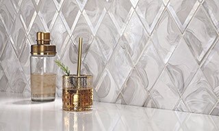 Dry bar with white & gray diamond-shaped backsplash, gold trimmed hi-ball glass and shaker on a white quartz countertop.