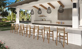 Resort outdoor bar with off-white subway tile backsplash, beige slab countertop, white tile base, wooden bar stools on brown pavers that look like stone.