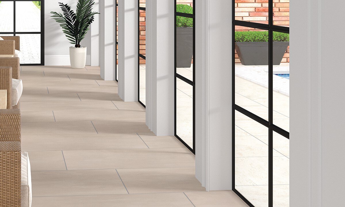 Closeup of hotel patio taupe floor tile that looks like concrete, outdoor pool with white pavers, and gray planters against brick wall.