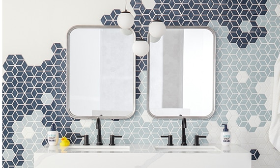 Bathroom with light blue, navy & and white cube mosaic tile backsplash and white porcelain slab countertop on double-sink vanity with black metal legs.
