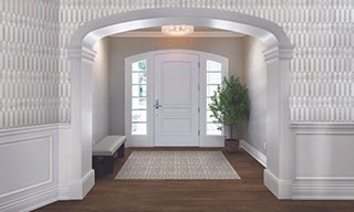 Traditional style home foyer with white and gray marble mosaic wall tile, floor tile that looks like dark wood planks, white front door with side windows.