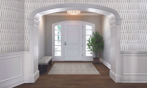 Traditional style home foyer with white and gray marble mosaic wall tile, floor tile that looks like dark wood planks, white front door with side windows.