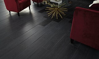 Closeup of black wood look tile accented by black geometric tile, crimson velvet chairs, and glass coffee table with gold base.