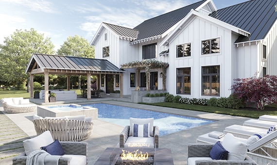 Modern farmhouse two-story home with white wood siding, black metal roof, pool with blue tile & gray deck that looks like stone, covered patio with couch and dining table.