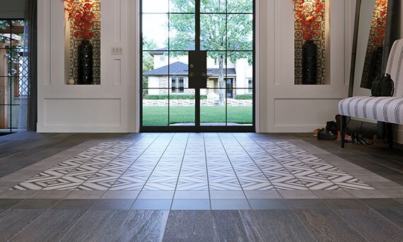 Modern farmhouse interior foyer with decorative encaustic-look tile and solid tile around the perimiter. Large glass doors in the background.