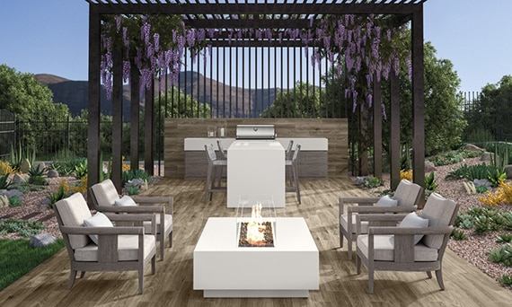 Outdoor patio / kitchen with floor tiles that look like wood, white porcelain slab island and firepit, stainless steel grill, and lavender hanging from pergola.