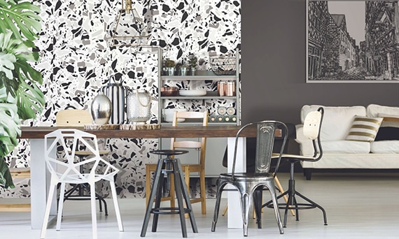 Open living room and dining room with feature wall made of white, gray, and black terrazzo look porcelain slab, table with mismatched chairs, and white sofa.