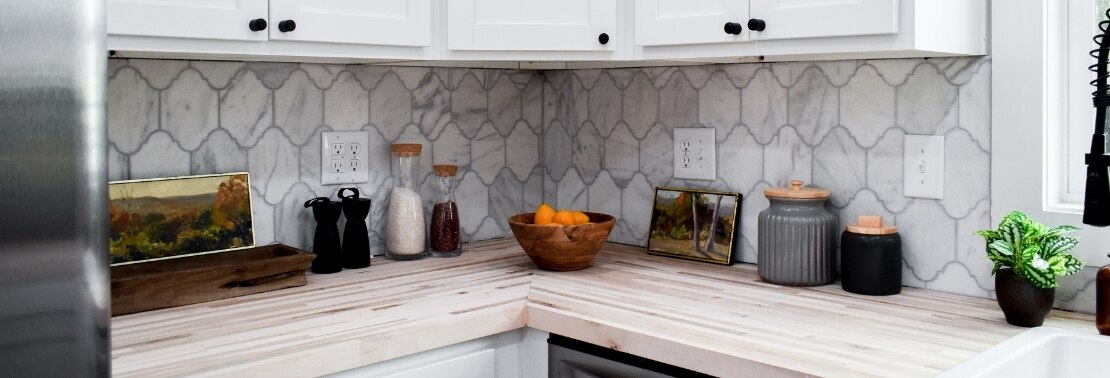 Kitchen backsplash of white & gray, Victorian mosaic marble tile, butcher block countertop, and white cabinets.