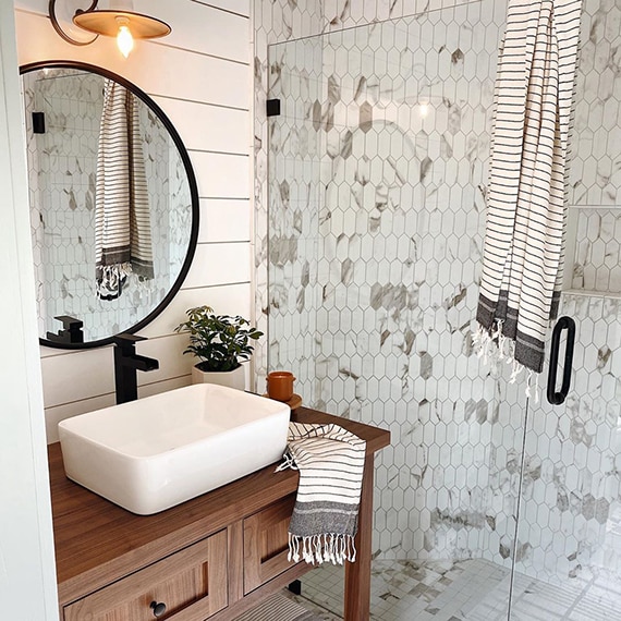 Newly renovated bathroom with white & gray picket shower wall tile, white & gray mosaic shower floor tile, white shiplap wall, wood vanity with white vessel sink.