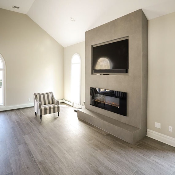 Newly renovated living room with floor tile that looks like wood, fireplace with porcelain slab that looks like metal façade and mounted flat-screen TV.