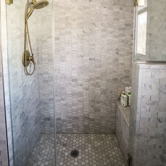 Shower with bench seat, gray marble picket mosaic shower wall tile, gray marble hexagon shower floor tile, and brass fixtures.
