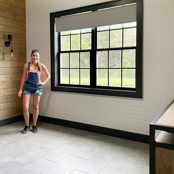 Newly renovated bedroom with gray floor tile that looks like concrete, natural wood wall, brick wall painted white, and windows with black trim.